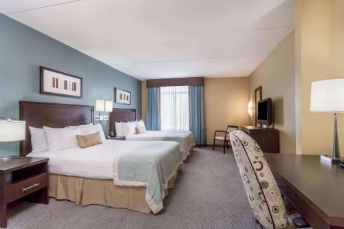 a hotel room with two beds and a desk at Wingate by Wyndham Regina in Regina