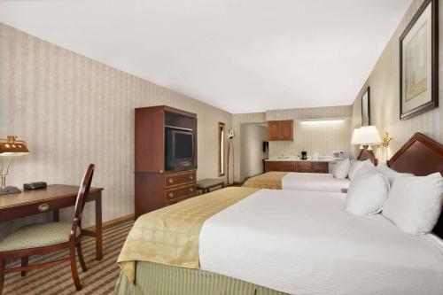 a hotel room with two beds and a desk at Ramada by Wyndham Saginaw Hotel & Suites in Saginaw
