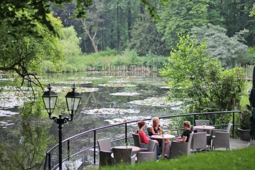 two women sitting at tables in front of a river at Hotel Erve Hulsbeek in Oldenzaal