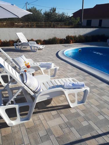 two white lounge chairs next to a swimming pool at Samodol in Drinovci