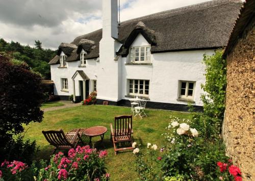 a white house with chairs and a table in the yard at Brook Farmhouse in Exeter