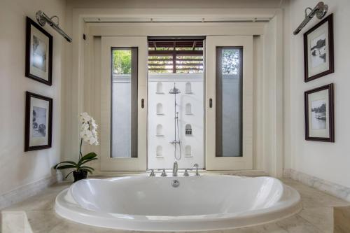 a large white tub in a bathroom with two windows at 137 Pillars House in Chiang Mai