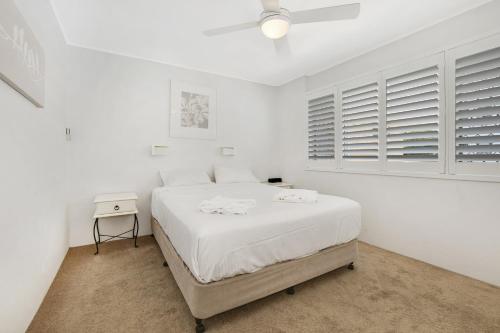 a white bedroom with a large bed and a table at 2 Bedroom Top Floor Unit - Ocean Views and Pool in Alexandra Headland