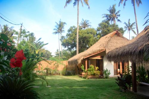 a house with a grass roof and some palm trees at Nanas Homestay in Gili Air