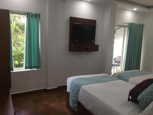 a bedroom with two beds and a television on the wall at Spice Villa Thekkady in Thekkady