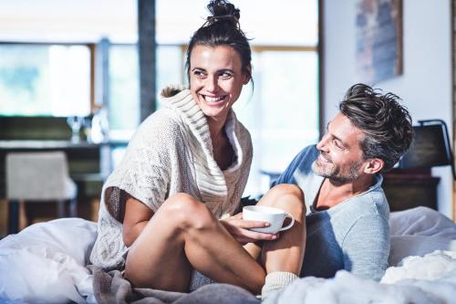 a man and woman sitting on a bed holding a cup at Hotel Klosterbräu in Seefeld in Tirol