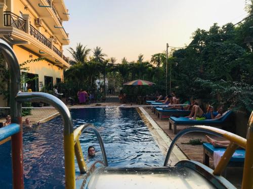 a swimming pool with people sitting on benches in a resort at Blue Diamond Hostel in Battambang
