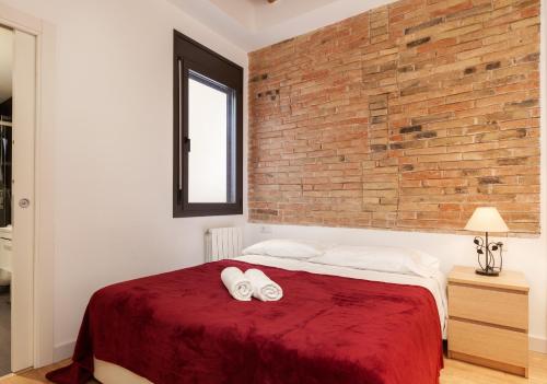 1 dormitorio con pared de ladrillo y 1 cama con 2 toallas en Akira Flats Urgell apartment, en Barcelona