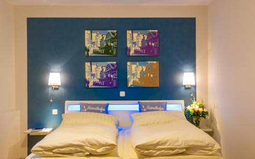a bedroom with a blue wall with paintings above a bed at Hotel Goldflair am Rathaus in Korbach