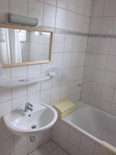 a white bathroom with a sink and a tub at Hotel Waldesruh in Düsseldorf