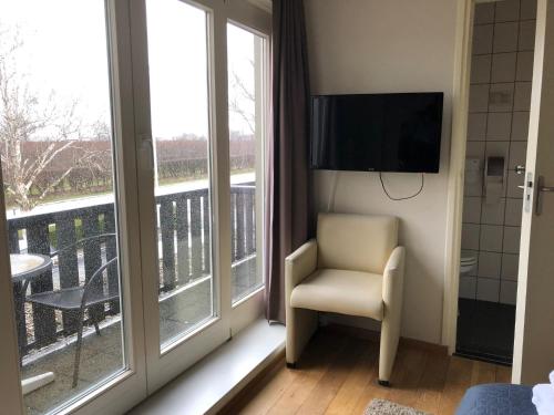 a room with a television and a chair and a balcony at Hotel de Plank - alle kamers met airconditioning in Noorbeek
