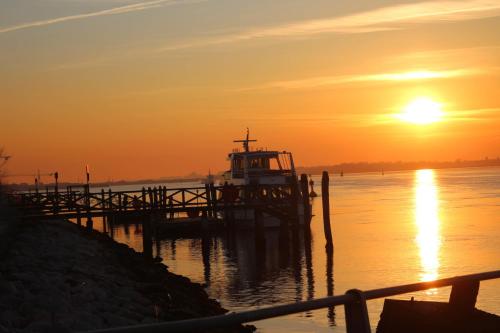 a dock with a boat in the water at sunset at La Brigata Apartments Orange House in Cavallino-Treporti