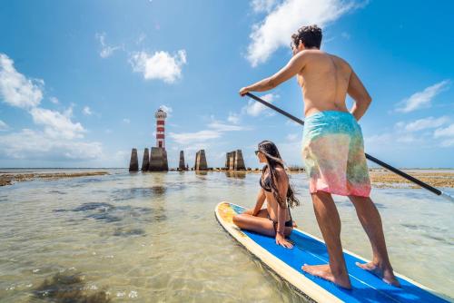 a man and a woman on a paddle board in the water at Hotel Brisa Praia Pajuçara in Maceió