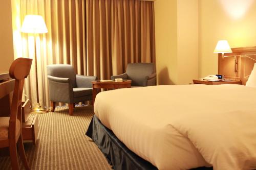 a hotel room with a bed and two chairs at HOTEL GRAND HILLS SHIZUOKA in Shizuoka