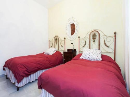una camera con 2 letti con lenzuola rosse e uno specchio di Apartamento Santa Cruz a Siviglia