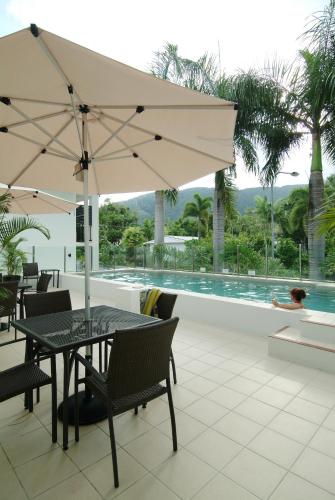 a patio with a table with an umbrella and a pool at Elysium Apartments in Palm Cove