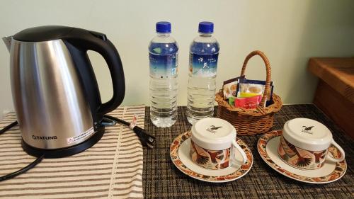 a tea kettle and two cups on a table with water bottles at Yi Tian Homestay in Fengli