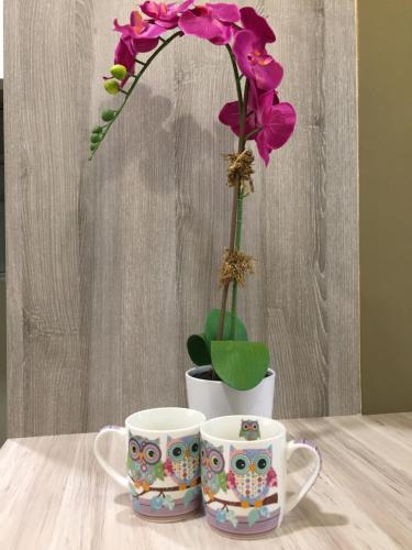 two cups on a table with a flower in a vase at Southville Stay 2 @ Savanna Executive Suite in Kampong Tangkas