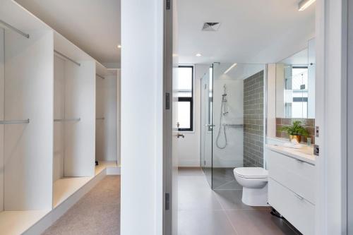 a white bathroom with a toilet and a shower at Blissful Breeze Townhouse with Parking and Patio in Auckland