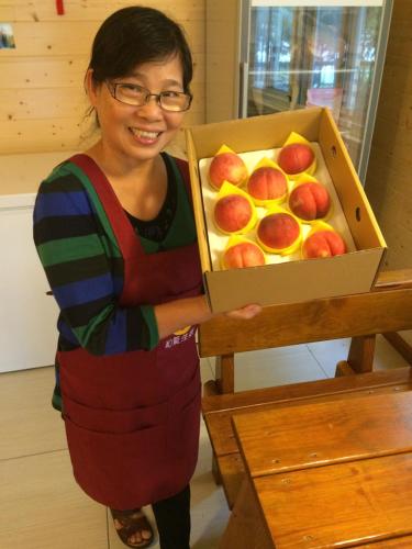 a woman is holding a box of peaches at He Feng Homestay in Hualing