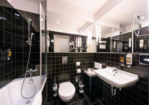 a black tiled bathroom with a toilet and a sink at Grandium Hotel Prague in Prague