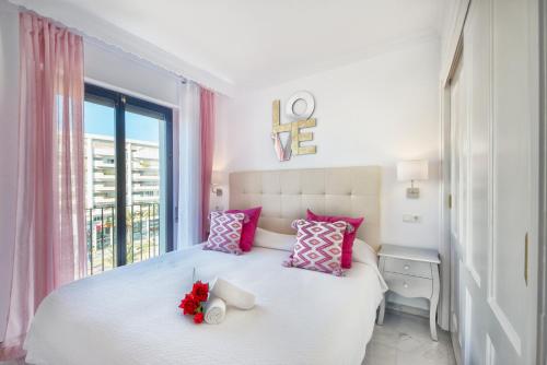 Un dormitorio con una cama blanca con almohadas rosas y una ventana en Jardines Del Puerto en Marbella