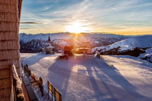 a snow covered mountain with a church in the sunset at Berghotel Schmittenhöhe - 2000m in Zell am See