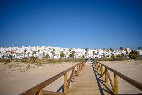 a wooden boardwalk over the beach with buildings in the background at Arena House Conil in Conil de la Frontera