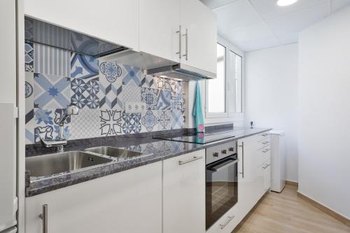 a kitchen with white cabinets and blue and white tiles at Pis Ocata in Masnou