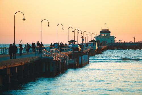 a group of people walking on a pier with a lighthouse at Quest St Kilda Bayside in Melbourne