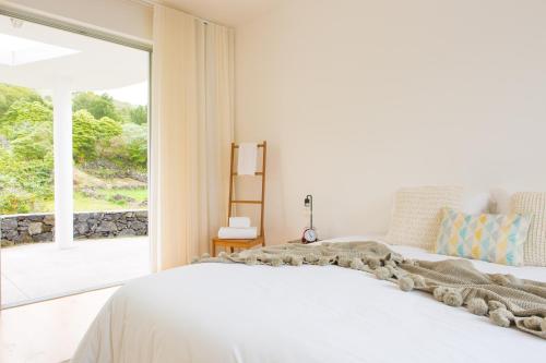 a bedroom with a white bed and a large window at Casa dos Caldeiras in Lajes do Pico