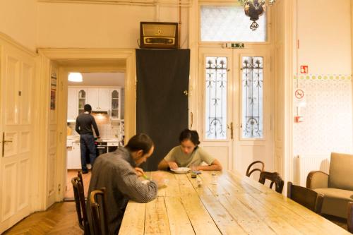 two people sitting at a wooden table in a room at Baroque Hostel & Coworking in Budapest