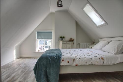 a white bedroom with a bed with a window at Huisje de Eersteling in Moddergat