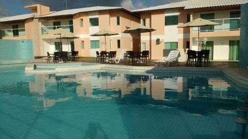 una piscina frente a un edificio con mesas y sombrillas en Casa Recanto de Guarajuba, en Guarajuba