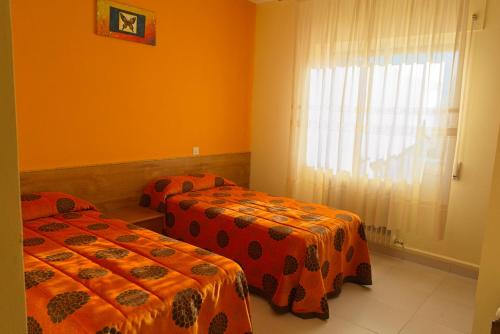 2 Betten in einem Zimmer mit orangefarbenen Wänden und einem Fenster in der Unterkunft Casa Rural El Negrillo in Ricobayo