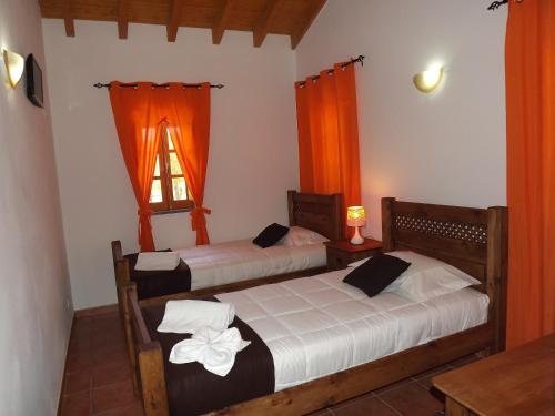 two beds in a room with orange curtains and a window at Casa de Campo Vale do Asno in Altura