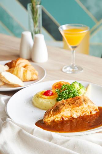 a table with two plates of food and a glass of orange juice at The Quarter Ladprao by UHG in Bangkok