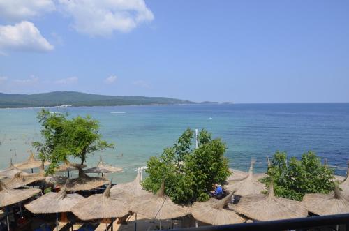 a group of straw umbrellas on a beach with the ocean at Ashram Hotel in Primorsko