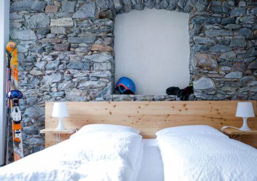 a bed with two pillows and a stone wall at Bed&Bike Tremola San Gottardo in Airolo