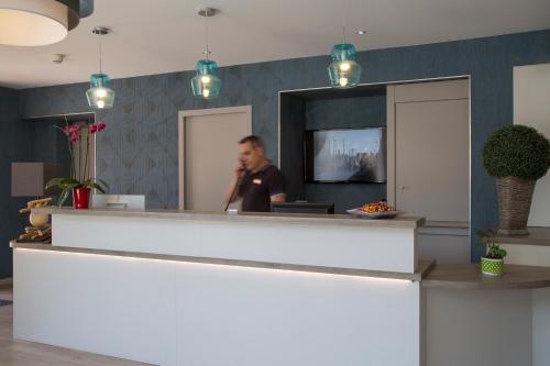 a man talking on a phone at a reception desk at The Originals City, Hôtel Le Boeuf Rouge, Saint-Junien in Saint-Junien