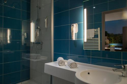 ein blau gefliestes Bad mit einem Waschbecken und einem Spiegel in der Unterkunft The Originals City, Hôtel Le Boeuf Rouge, Saint-Junien in Saint-Junien