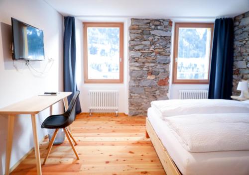 a bedroom with a bed and a desk and windows at Bed&Bike Tremola San Gottardo in Airolo