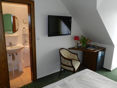 Garni Hotel Moselschild في أورزيغ: غرفة نوم مع سرير ومكتب مع تلفزيون على الحائط