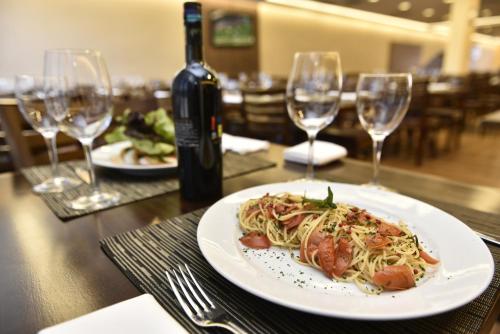 a plate of pasta on a table with wine glasses at Hotel Rainha do Brasil in Aparecida