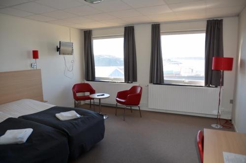 a hotel room with a bed and two chairs and windows at Nattoralik in Aasiaat