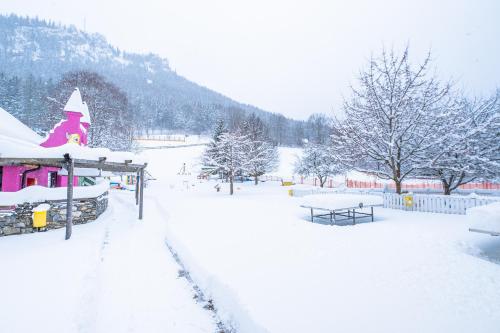 a snow covered park with a pink building and trees at Kinderhotel Appelhof in Mürzsteg