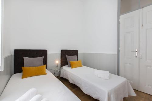 Faro Cosy Guesthouse في فارو: سريرين في غرفة مع وسائد بيضاء وصفراء