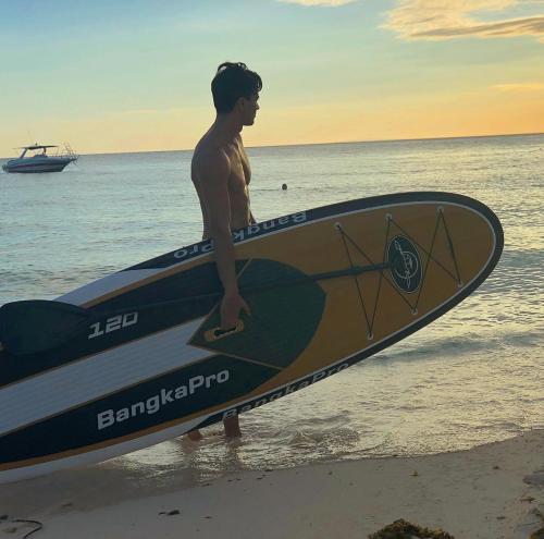 a man standing on the beach holding a surfboard at Crimson Resort and Spa Boracay in Boracay