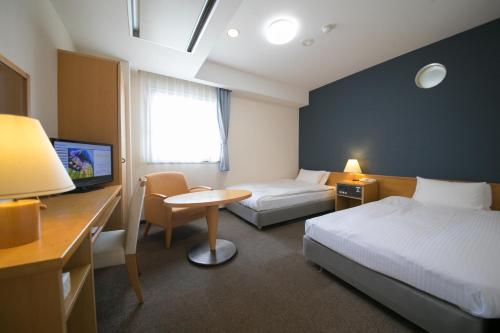 Habitación de hotel con cama, escritorio y TV. en Heiwadai Hotel 5, en Fukuoka