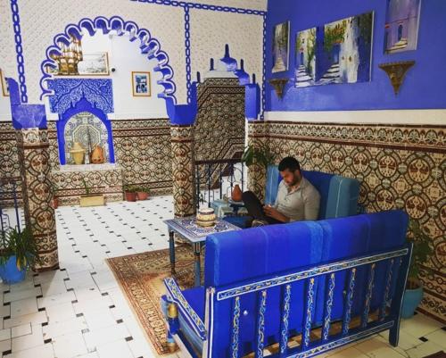 a man sitting on a blue couch with a laptop at Hotel Abi khancha in Chefchaouen